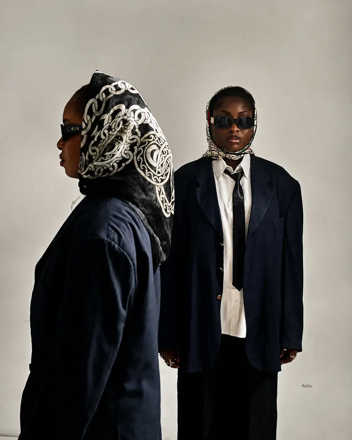 Two models in dark tailoring and patterned head scarves
